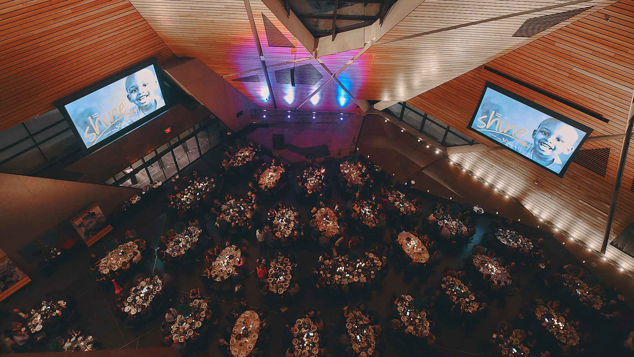 Overhead of a large dark room filled with gala attendees and two screens